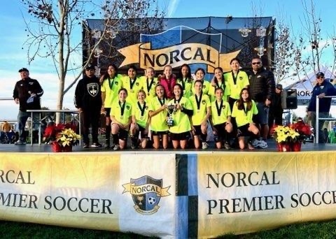 Sentinels girls competitive team lifting their trophy on the NorCal Premier Soccer championship stage